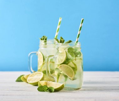 Mojito limes ve ahşap masa üzerinde cam kavanozlara nane kokteyli. Mavi arka plan