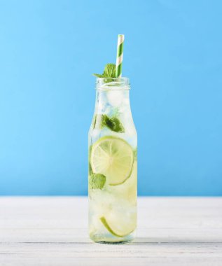 Mojito kokteyl limon ve nane Beyaz ahşap masa üzerinde cam şişede. Mavi arka plan