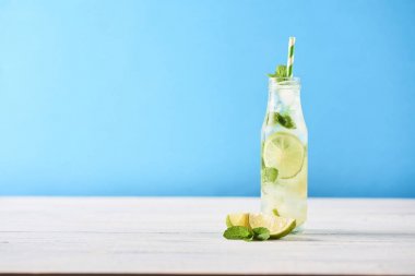 Mojito kokteyl limon ve nane Beyaz ahşap masa üzerinde cam şişede. Mavi arka plan. Metin için yer