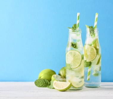 Mojito kokteyl limon ve nane Beyaz ahşap masa üzerinde cam şişelerde. Mavi arka plan. Metin için yer