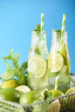 Mojito kokteyl limon ve nane Beyaz ahşap masa üzerinde cam şişelerde. Mavi arka plan