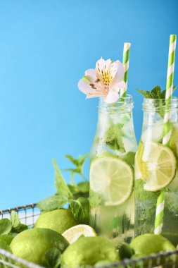 Mojito kokteyl limon ve nane Beyaz ahşap masa üzerinde cam şişelerde. Mavi arka plan