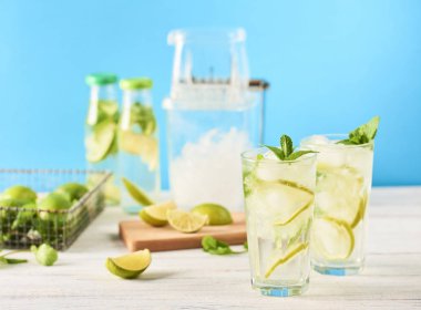 Mojito limes ve beyaz tahta masada highball bardaklarda nane kokteyli. Mavi arka plan
