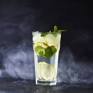 Mojito limes ve highball cam dumanlı karanlık taş zemin üzerine nane kokteyli.
