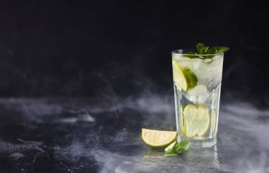 Mojito limes ve highball cam dumanlı karanlık taş zemin üzerine nane kokteyli.