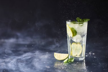 Mojito limes ve highball cam dumanlı karanlık taş zemin üzerine nane kokteyli.