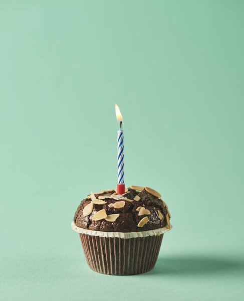 Вкусный шоколадный кекс со свечой на бирюзовом фоне. Минимальная концепция
