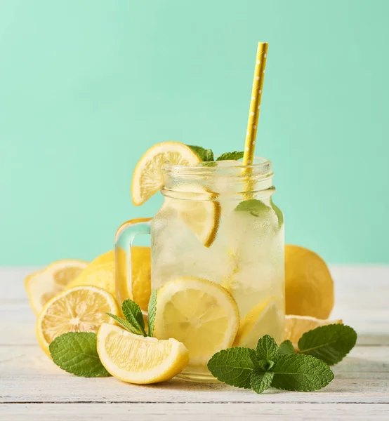 Fresh tasty lemonade in mason jar glass on wooden table over turquoise background