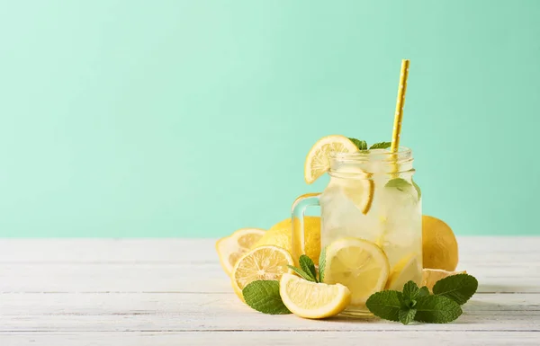 Fresh tasty lemonade in mason jar glass on wooden table over turquoise background