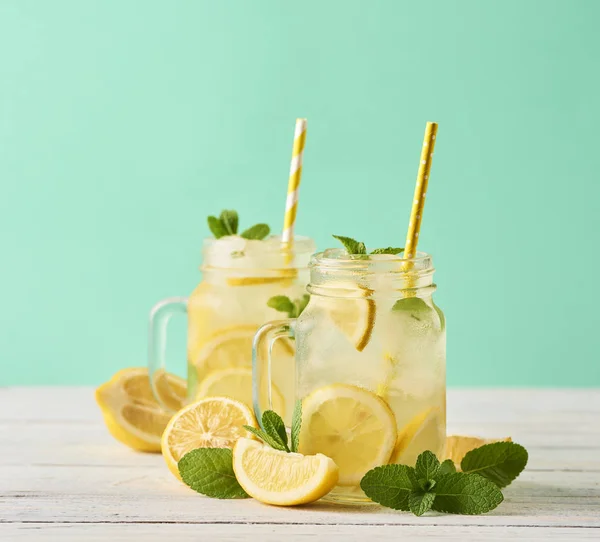 Fresh tasty lemonade in mason jars on wooden table over turquoise background