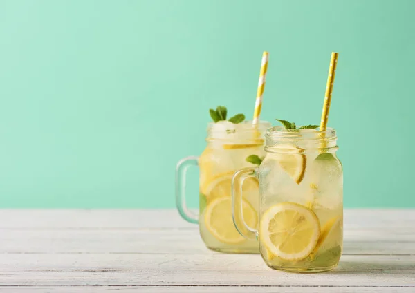 Fresh tasty lemonade in mason jars on wooden table over turquoise background