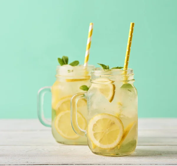 Fresh tasty lemonade in mason jars on wooden table over turquoise background