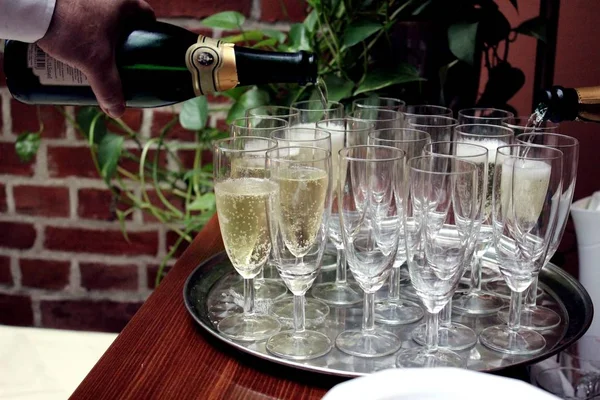 Close-up van een sterke waiter's hand gieten alcohol champagne in een glazen op een dienblad — Stockfoto