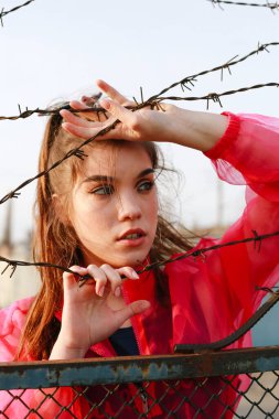Dikenli tellerin arkasında elinde bir tel tutan kız daha iyi bir gelecekte güneşe bakıyor.