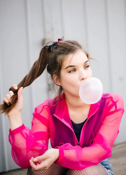 The girl blow up inflates a bubble of chewing gum in pink blouse street style trendy portrait