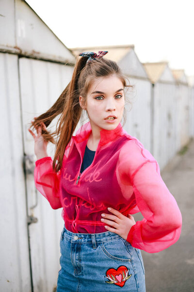 Образцовая молодая женщина / девушка в розовой блузке позирует в гаражах. Трендовый портрет в уличном стиле