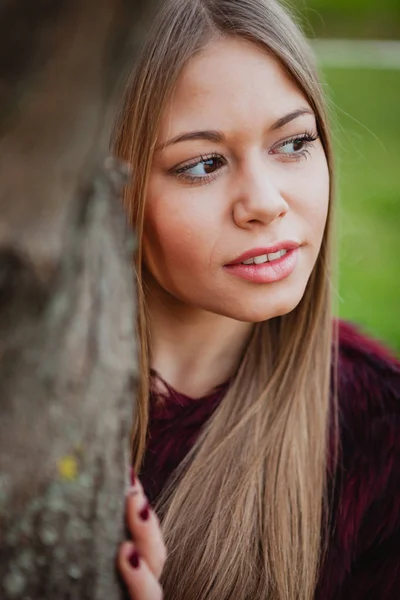 Blonde girl next to tree trunk — Stock Photo, Image