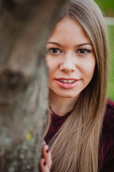 Blonde girl next to tree trunk — Stock Photo, Image