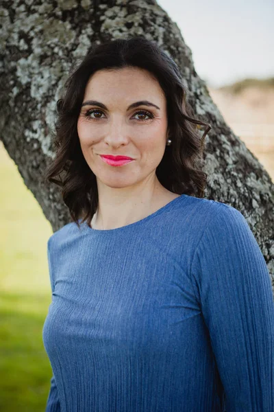 Woman in blue dress leaning on tree — Stock Photo, Image