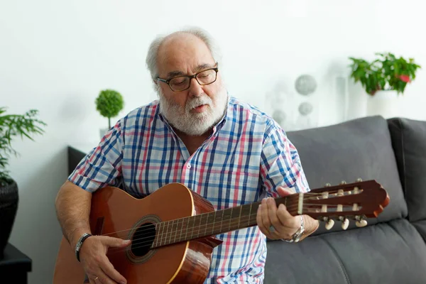 portrait of senior man with white beard playing guitar at home