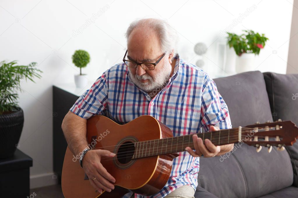 portrait of senior man with white beard playing guitar at home 