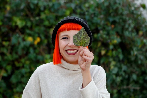 attractive young woman in cap showing green leaf in park