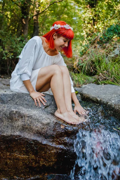 白いドレスと滝の近くに座っての花輪を身に着けている美しい若い女性 — ストック写真