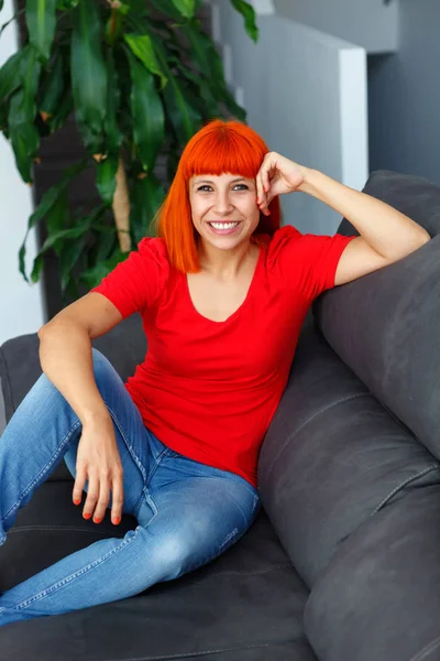 快乐美丽的红衫女郎穿着红色 T恤摆在家里坐在沙发上 — 图库照片