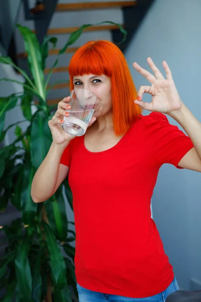 Ruiva Mulher Feliz Roupas Vermelhas Beber Água Mostrando Gesto — Fotografia de Stock