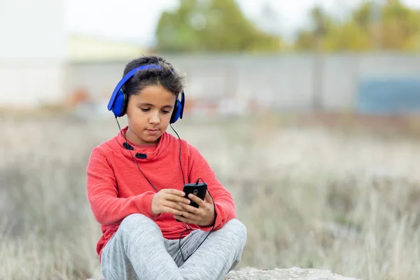 Дитина з темним волоссям слухає музику з синіми навушниками і м — стокове фото