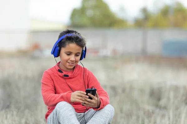 Niño con cabello oscuro escuchando música con hadphones azules y un m —  Fotos de Stock