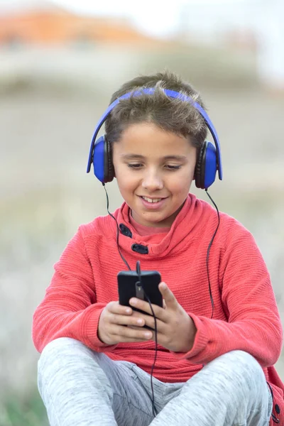 Niño con cabello oscuro escuchando música con hadphones azules y un m — Foto de Stock