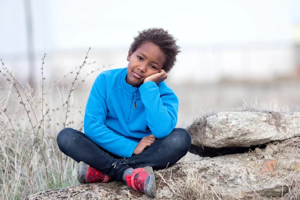 Gelangweiltes Kind sitzt auf einem Felsen im Grünen — Stockfoto