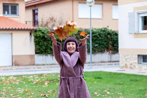 Mor ceketli mutlu kadın yaprakları fırlatıyor. — Stok fotoğraf