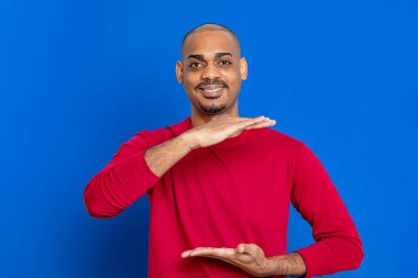 Kırmızı tişörtlü, mavi arka planda Afrikalı bir adam.