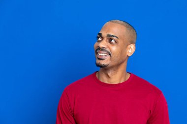 Kırmızı tişörtlü, mavi arka planda Afrikalı bir adam.