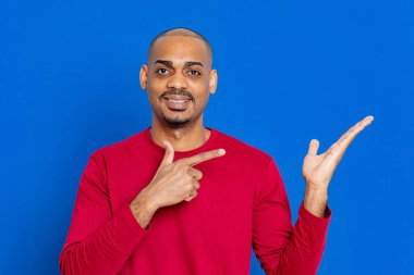Kırmızı tişörtlü, mavi arka planda Afrikalı bir adam.