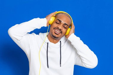 Mavi arka planda beyaz bir kazak giyen Afrikalı adam.