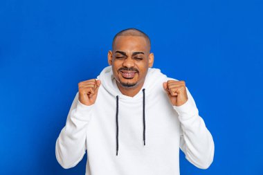 Mavi arka planda beyaz bir kazak giyen Afrikalı adam.