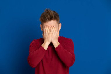 Mavi arka planda kırmızı tişörtlü çekici bir genç.