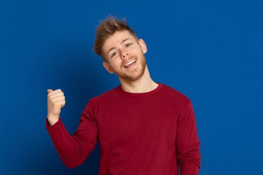 Mavi arka planda kırmızı tişörtlü çekici bir genç.