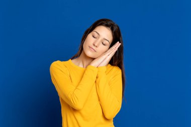 Esmer kız mavi arka planda sarı bir tişört giyiyor.