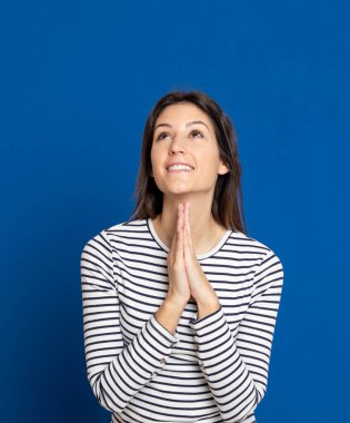 Mavi arka planda çizgili tişört giyen esmer genç bir kadın.