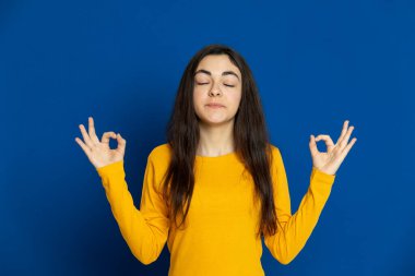 Esmer genç kız mavi arka planda sarı forma giyiyor.