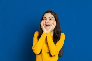 Esmer genç kız mavi arka planda sarı forma giyiyor.