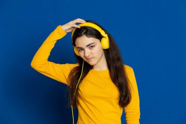 Esmer genç kız mavi arka planda sarı forma giyiyor.