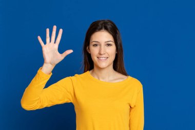 Esmer genç bir kadın, mavi arka planda sarı bir tişört giyiyor.