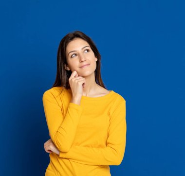 Esmer genç bir kadın, mavi arka planda sarı bir tişört giyiyor.