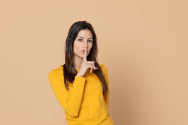 Sarı arka planda sarı tişört giyen esmer genç bir kadın.