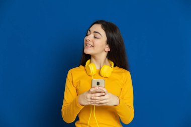 Esmer genç kız mavi arka planda sarı forma giyiyor.